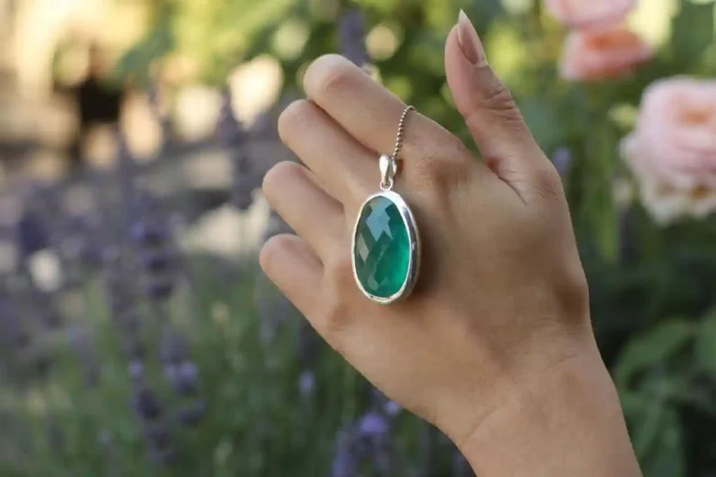 main de femme qui porte un pendentif avec une pierre imitation émeraude